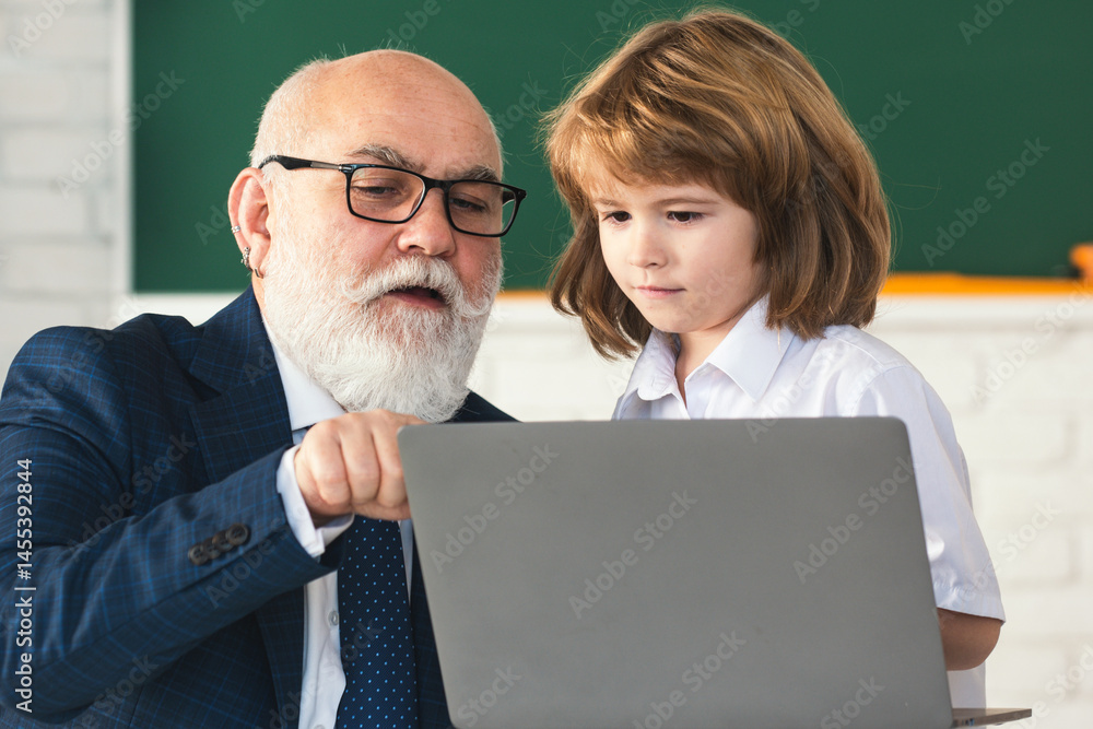 Portrait of senior teacher and school child. Mature teacher helps school child learn. School teacher and child in classroom. Teacher in school on lesson teach child on laptop.