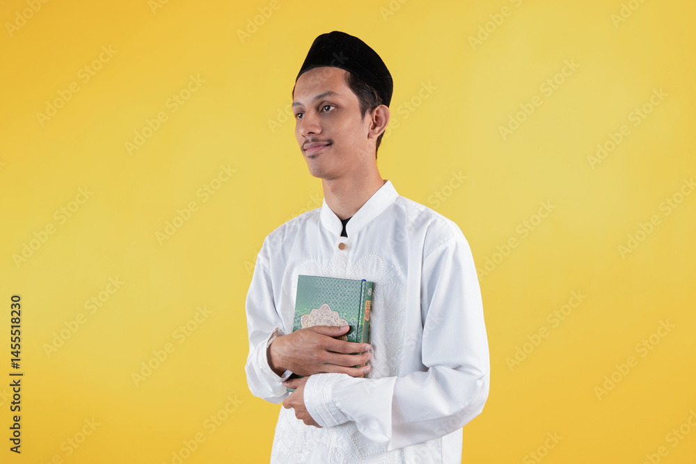 Smiling muslim man wear white shirts with Islamic ornaments while holding Holy book of Quran Smiling muslim man wear white shirts with Islamic ornaments while holding Holy book of Quran