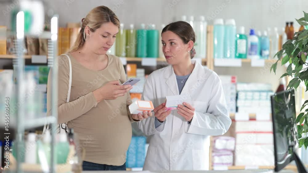 Interested expecting mother scanning QR codes on supplement boxes at drugstore, comparing two products, while smiling female pharmacist explaining benefits for fetal development Interested expecting mother scanning QR codes on supplement boxes at drugstore, comparing two products, while smiling female pharmacist explaining benefits for fetal development