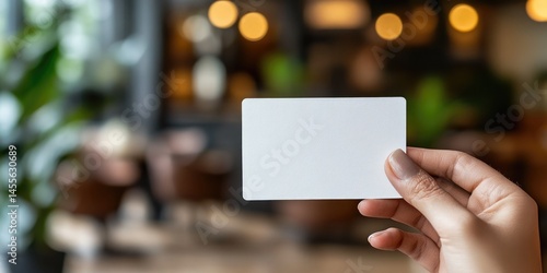 Hand holding blank white card (business/credit/gift card mockup), blurred cafe/restaurant background. Use for business or payment-themed sites.