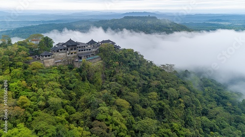 Scenic aerial vista of a forested hillside partially shrouded in mist with distant mountain range and a historic structure in the center