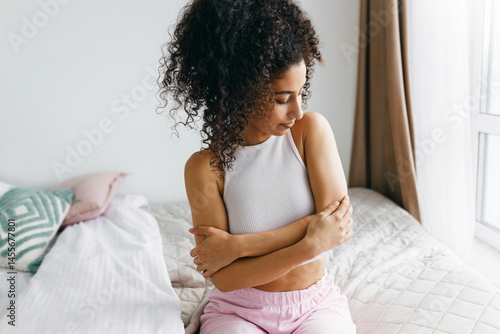 Fotografie Indoor cropped image of mulatto girl in tank top hugging herself around shoulder
