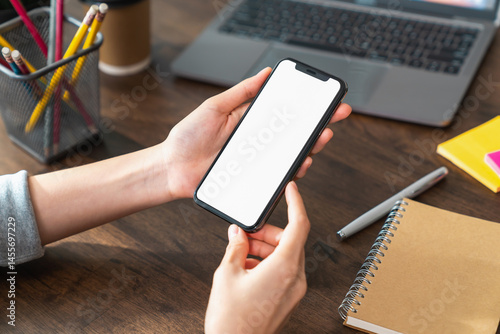 Hand holding smartphone with a blank screen on table, for putting advertising to promote.