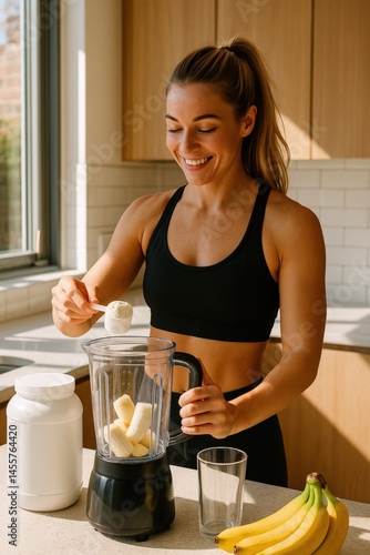 Smiling fit woman in sportswear preparing banana protein shake in blender on sunny kitchen counter