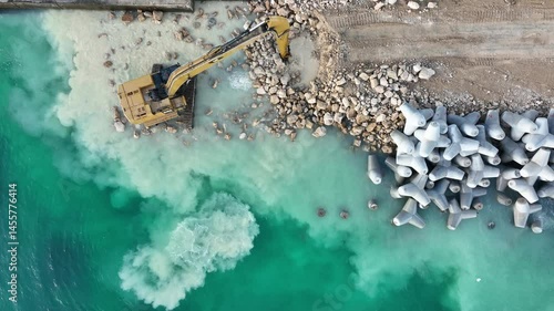 Aerial view of waterfront construction site with excavator. Excavator working on a breakwater construction
