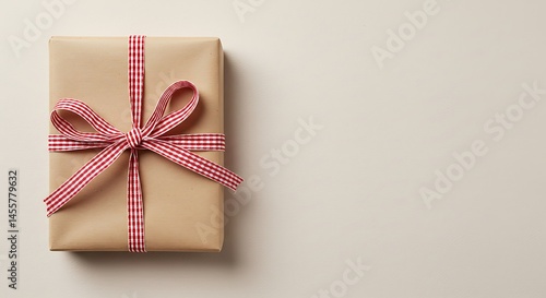 Gift box wrapped in brown paper with red ribbon on beige background  
