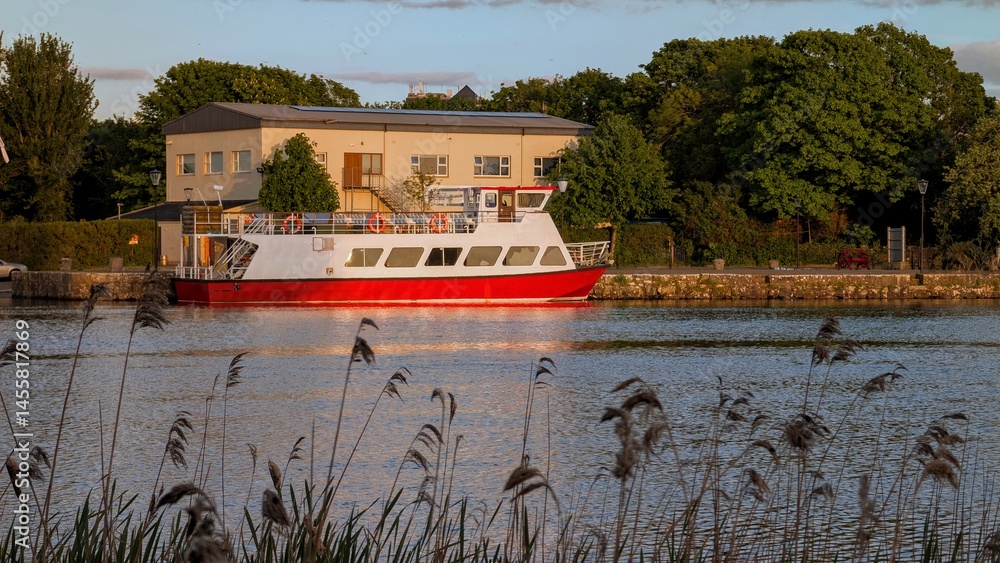 Red white boat in Corrib river at sunset, Galway city, Ireland, watercraft transportation, buildings and architecture, nature background