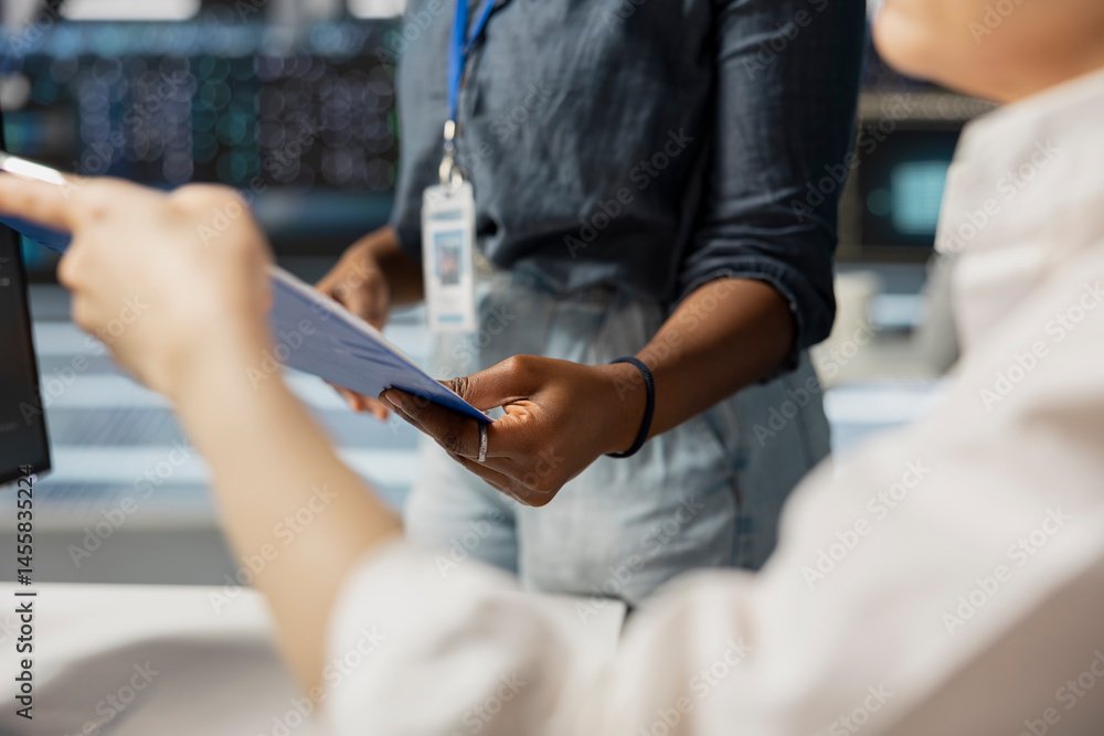 Close up of server room employees reviewing documentation on clipboard ahead of scheduled system audit. Data center coworkers verifying configuration data and compliance standards in office