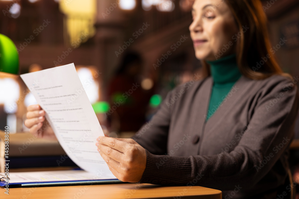 Aged focused woman in a public library studying educational materials and reading, representing preparation required for coursework and school exams. Learning from archived files. Close up.
