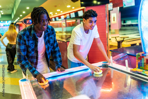 Two young men playing air hockey in entertainment center