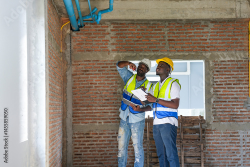 Wallpaper Mural Two construction inspectors reviewing plumbing and electrical systems on-site, checking building infrastructure and installation quality at a brick wall construction site. Torontodigital.ca