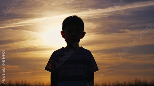 Young boy stands in the middle of a cloudy sky, looking up at the sun. Concept of solitude and contemplation, as the boy seems to be lost in thought