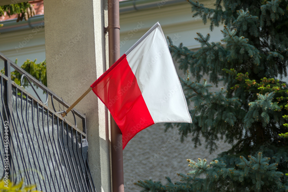 Biało czerwona flaga Polski umocowana na balustradzie balkonu.