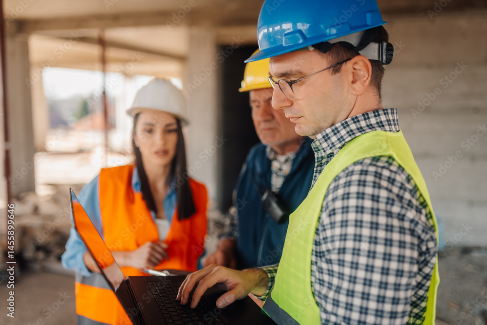 Engineers using laptop computer discussing project at construction site Engineers using laptop computer discussing project at construction site