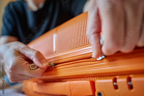 Fotografia Close-up of hands zipping orange suitcase before trip