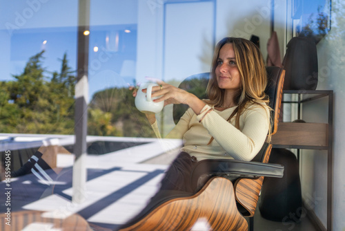 Woman by the window at home, with tea or coffee mug on her hand. Good morning, feeling good