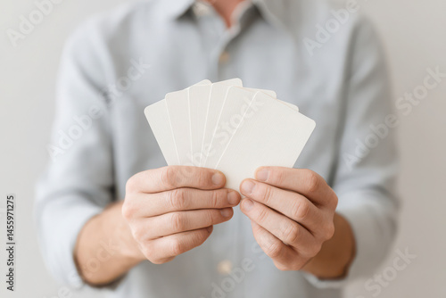 person holding playing cards in their hands against light background with soft lighting focusing on cards