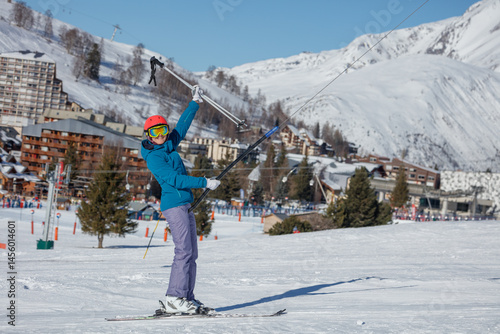 Happy skier woman on ski lift with mountain resort in backdrop