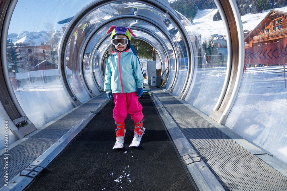 Child in colorful ski gear rides a tunnel lift at snowy resort
