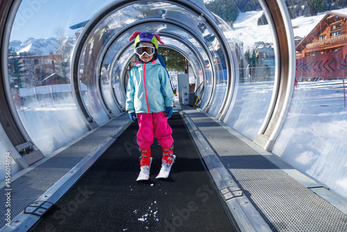Obraz na płótnie Child in colorful ski gear rides a tunnel lift at snowy resort w salonie