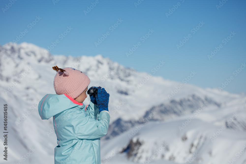 Child girl exploring snowy mountain landscape with binoculars