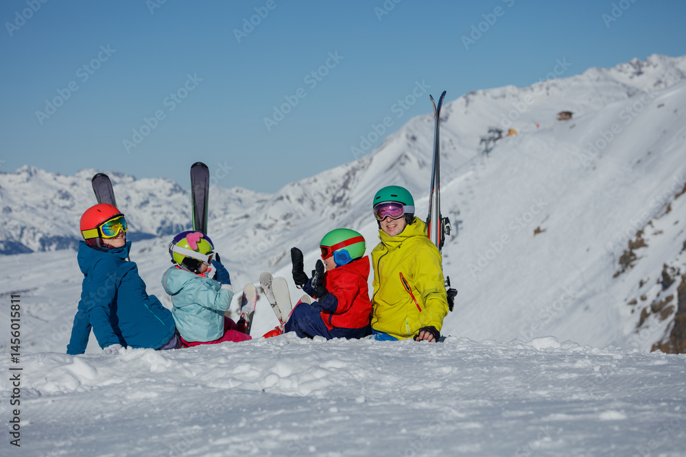Four people, prepared for skiing, sit on a snow-covered slope