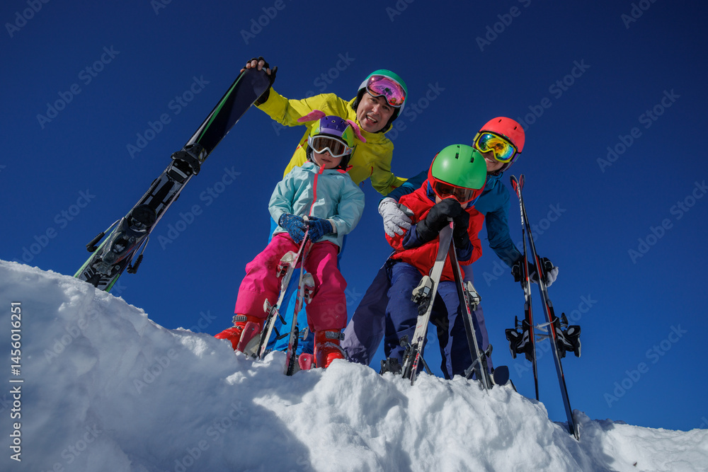 Family in bright ski gear smile at snowy mountains and blue sky