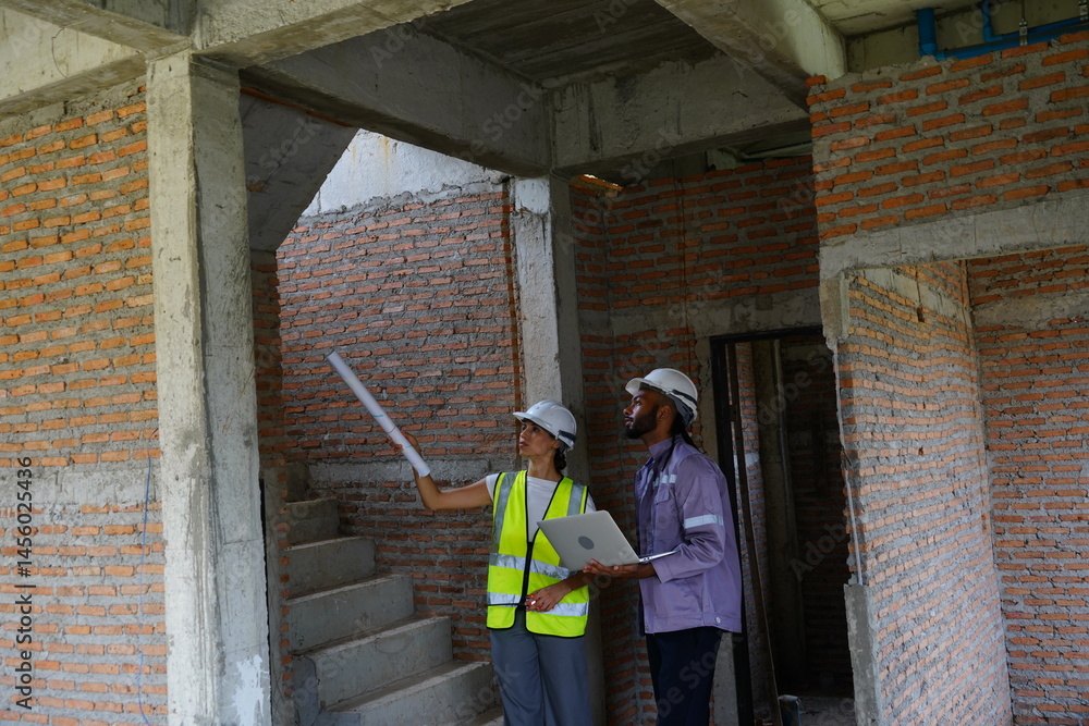 Black male engineer as foreman and Latin female construction inspector wearing construction helmet standing holding walkie talkie talking and consulting on construction of house project