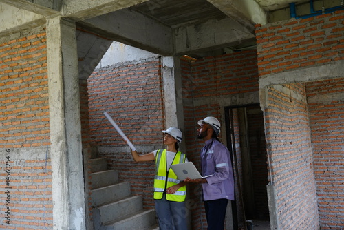 Obraz na płótnie Black male engineer as foreman and Latin female construction inspector wearing construction helmet standing holding walkie talkie talking and consulting on construction of house project w salonie