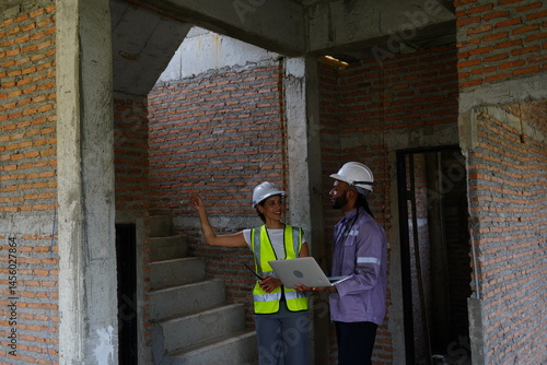 Obraz na płótnie Black male engineer as foreman and Latin female construction inspector wearing construction helmet standing holding walkie talkie talking and consulting on construction of house project w salonie