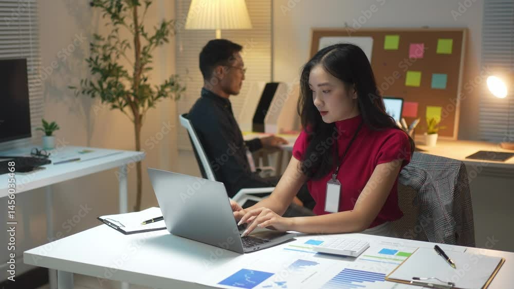 A woman is typing on a laptop in front of a bulletin board with a lot of notes on it A woman is typing on a laptop in front of a bulletin board with a lot of notes on it