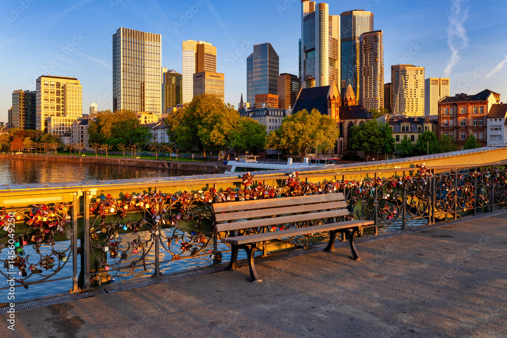 A bench in soft sunrise light on the footbridge Eiserner Steg in front of the city skyline, Frankfurt, Germany