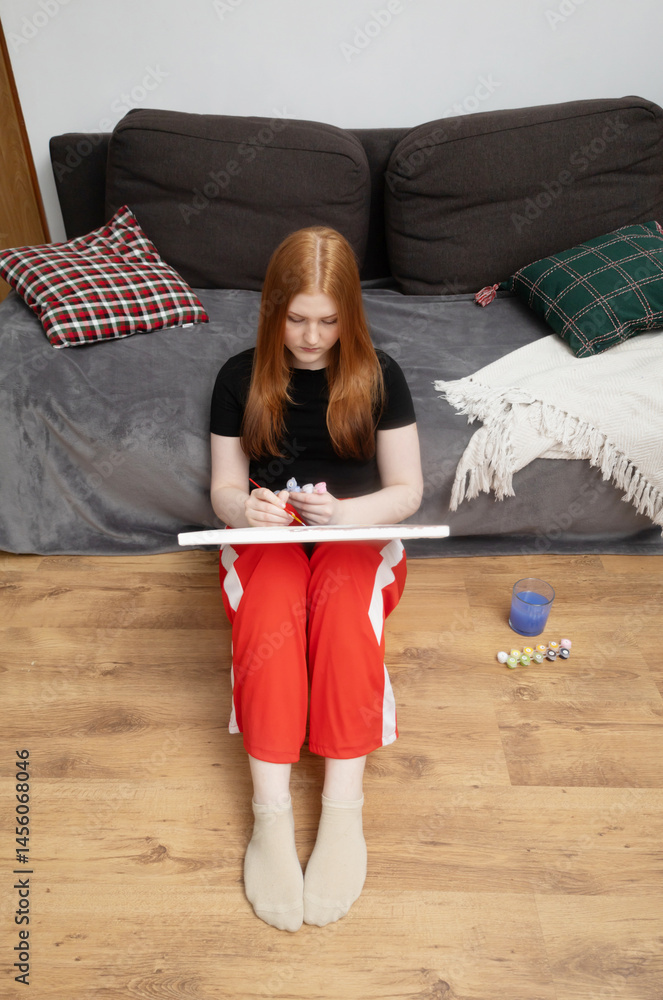 girl sitting on the floor at home and painting a picture by numbers painting by numbers