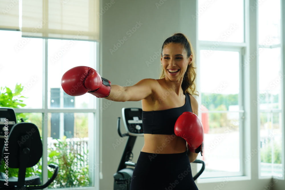 Beautiful young latin American woman in black sports bra exercising with red boxing gloves practicing boxing and punching in the gym. Health and weight loss concept.
