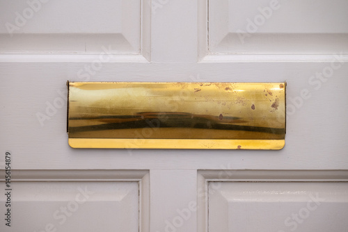 Close up of a gold-colored letter box on a white door. Old and worn.