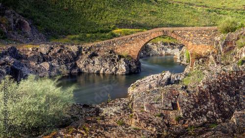Panoramic view of the beautiful Charcos bridge over the Isna river on the border of the municipalities of Sertã and Vila de Rei in Portugal, illuminated by the sunlight in the late afternoon.