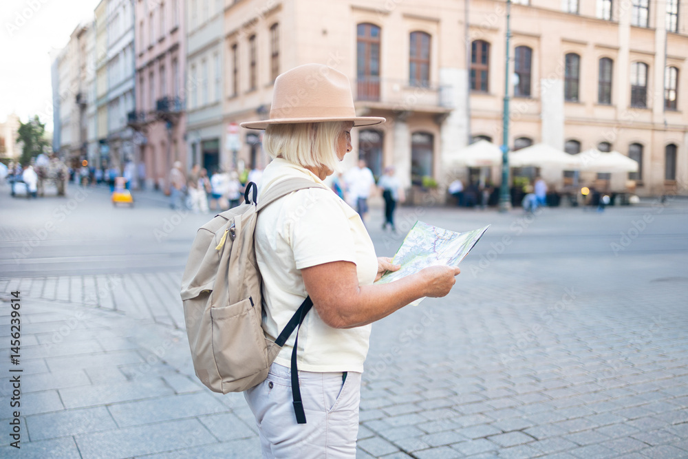 A senior woman stands in a beautiful city square, holding a map while enjoying sightseeing. She is dressed in a comfortable outfit, wearing a hat and sunglasses.