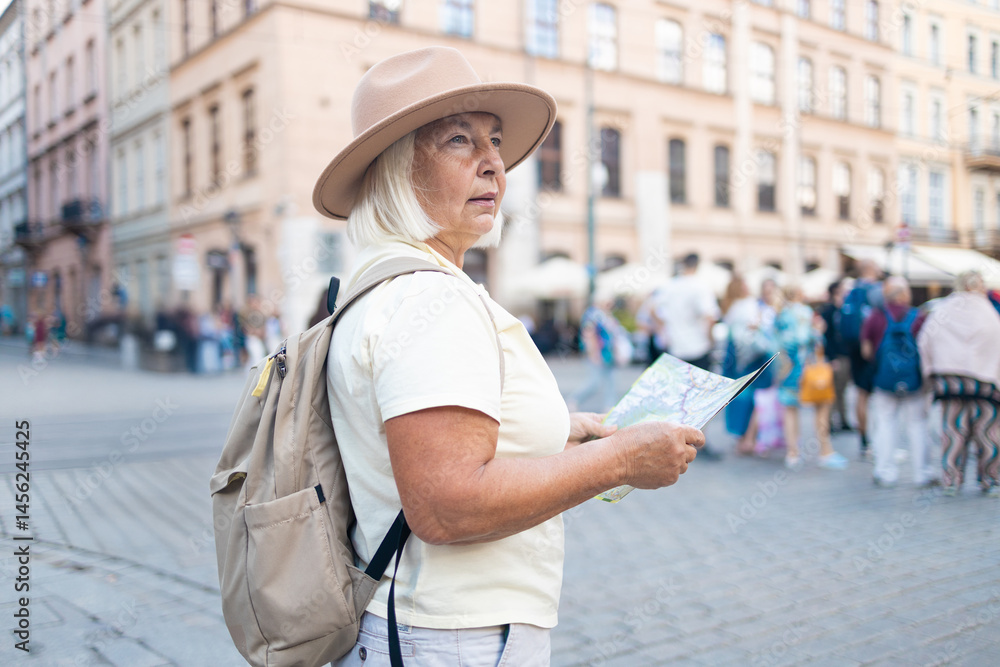 A senior woman stands in a beautiful city square, holding a map while enjoying sightseeing. She is dressed in a comfortable outfit, wearing a hat and sunglasses.