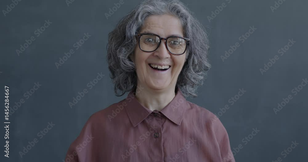 Slow motion portrait of excited and surprised senior woman looking at camera on gray color background. People and positive emotion concept. Slow motion portrait of excited and surprised senior woman looking at camera on gray color background. People and positive emotion concept.