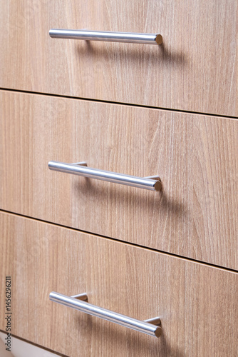 Rectangle shaped kitchen cabinet with stainless steel brushed handles close up selective focus shot. Cabinet door adorned with metal handles