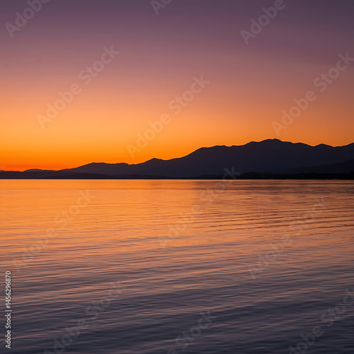 Sunset over calm water, mountains in silhouette.