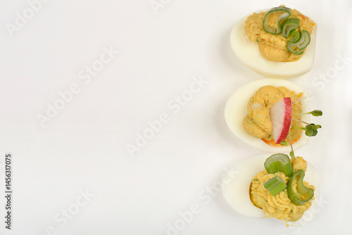 Three deviled egg halves, each uniquely garnished with celery, radish, and sprouts, are presented on a white plate
