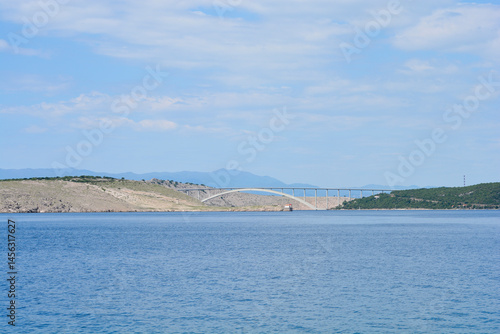 Obraz na płótnie A scenic view from Jadranovo captures the Krk Bridge spanning the blue sea, connecting the mainland to Krk Island under a partly cloudy sky w salonie