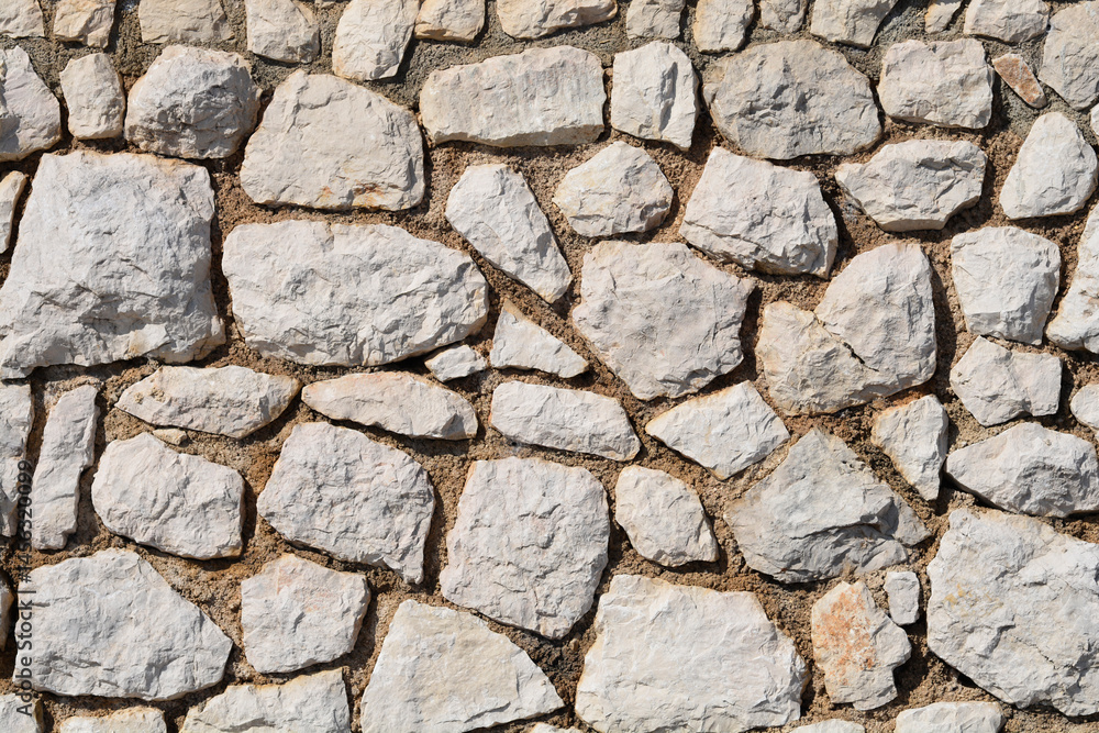 A textured stone wall is constructed from irregularly shaped, light-colored rocks and mortar