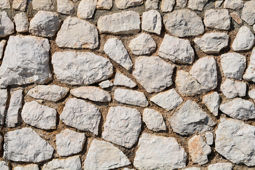 Obraz na płótnie A textured stone wall is constructed from irregularly shaped, light-colored rocks and mortar w salonie