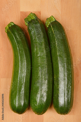 Obraz na płótnie Three green zucchinis are arranged vertically on a light brown wooden surface w salonie