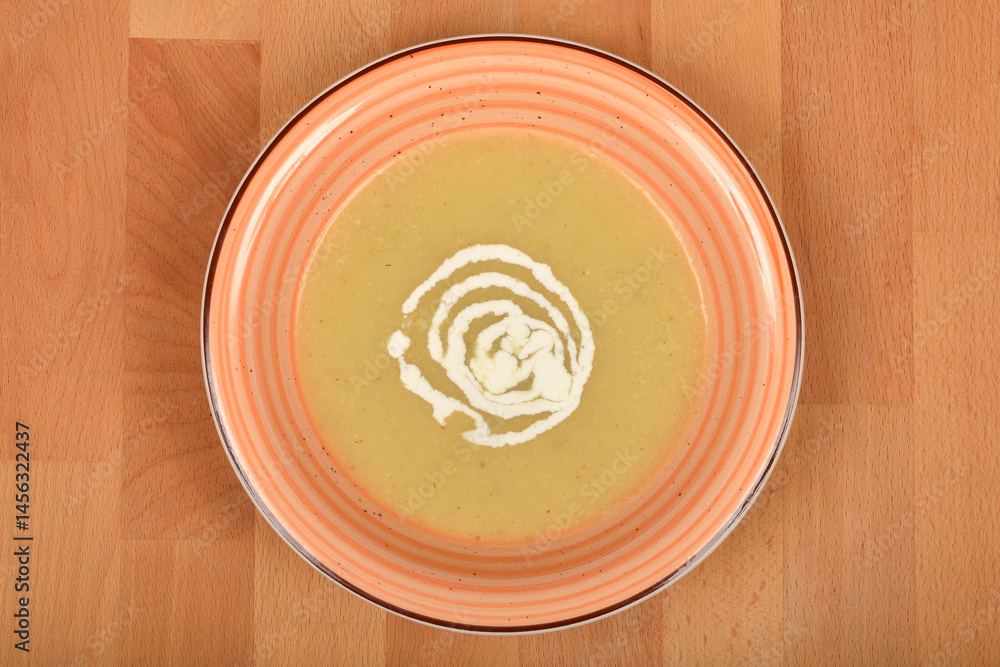 A top-down close-up shows a bowl of creamy parsnip soup garnished with a swirl of cream on a striped plate, set on a wooden surface