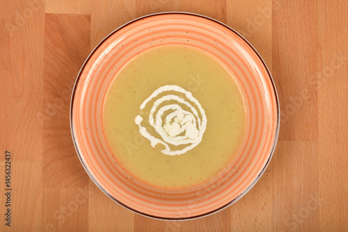 Obraz na płótnie A top-down close-up shows a bowl of creamy parsnip soup garnished with a swirl of cream on a striped plate, set on a wooden surface w salonie