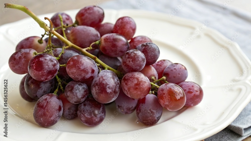 Fototapeta premium A cluster of purple grapes on a white ceramic plate.