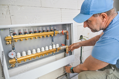Obraz na płótnie A dedicated plumber is carefully configuring a modern plumbing control setup, ensuring precise performance of the home's plumbing system with specialized tools w salonie